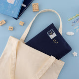 Cloud Dreamland notebook pouch peaking out of a plain canvas tote bag