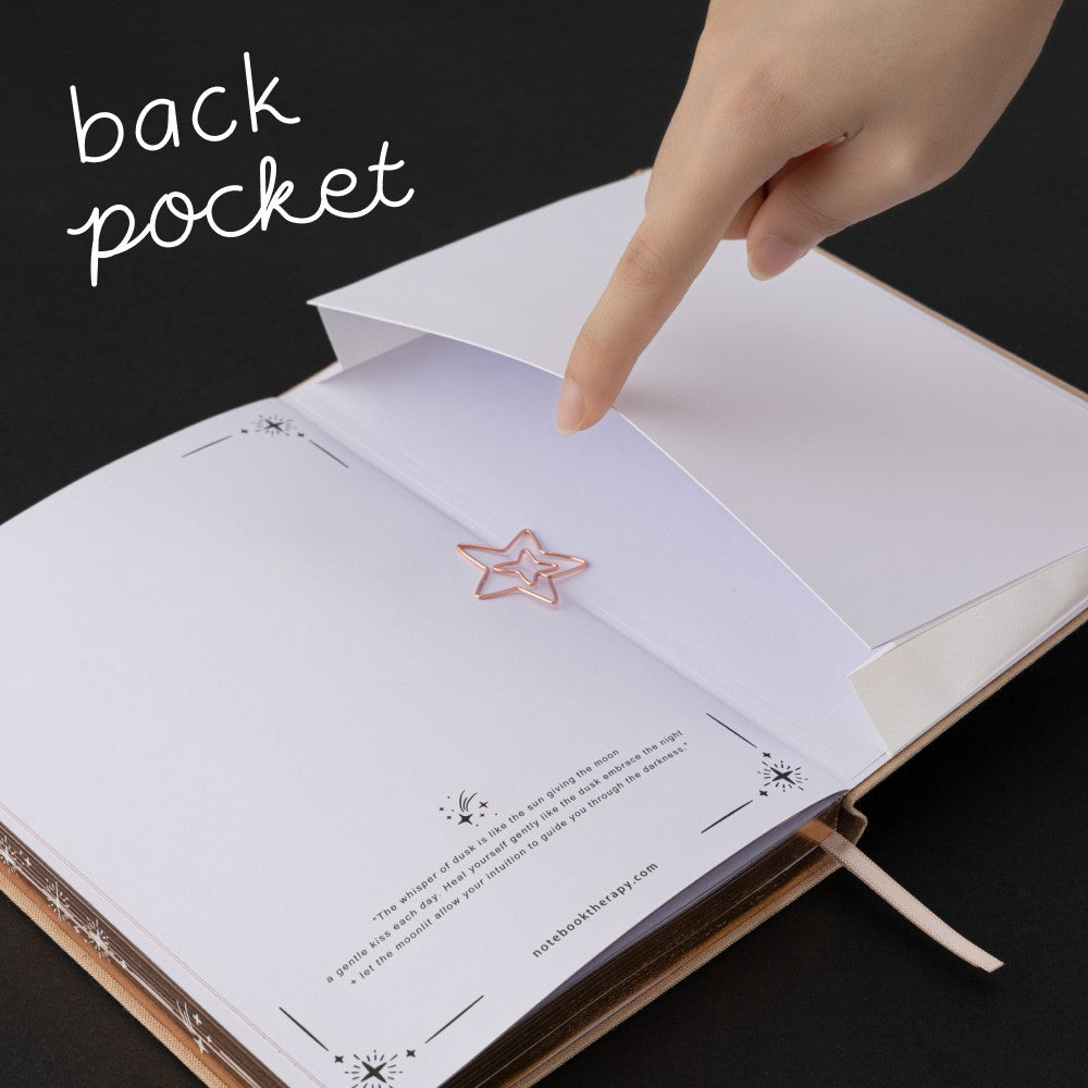 Hand opening the back pocket of Tsuki Stardust Dawn Bullet Journal with rose gold star-shaped paperclip inside