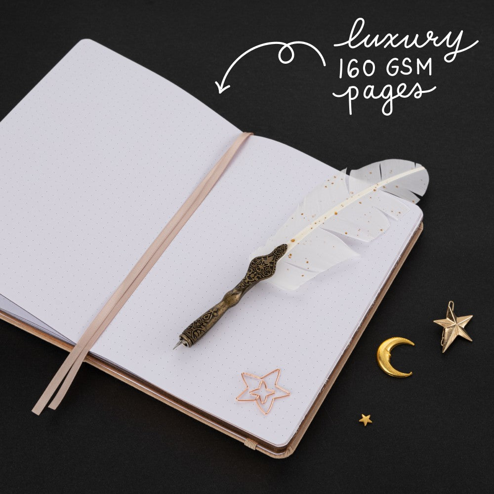 Feather quill and rose gold star-shaped paperclip on white page dotted notebook with lettering “luxury 160gsm pages”