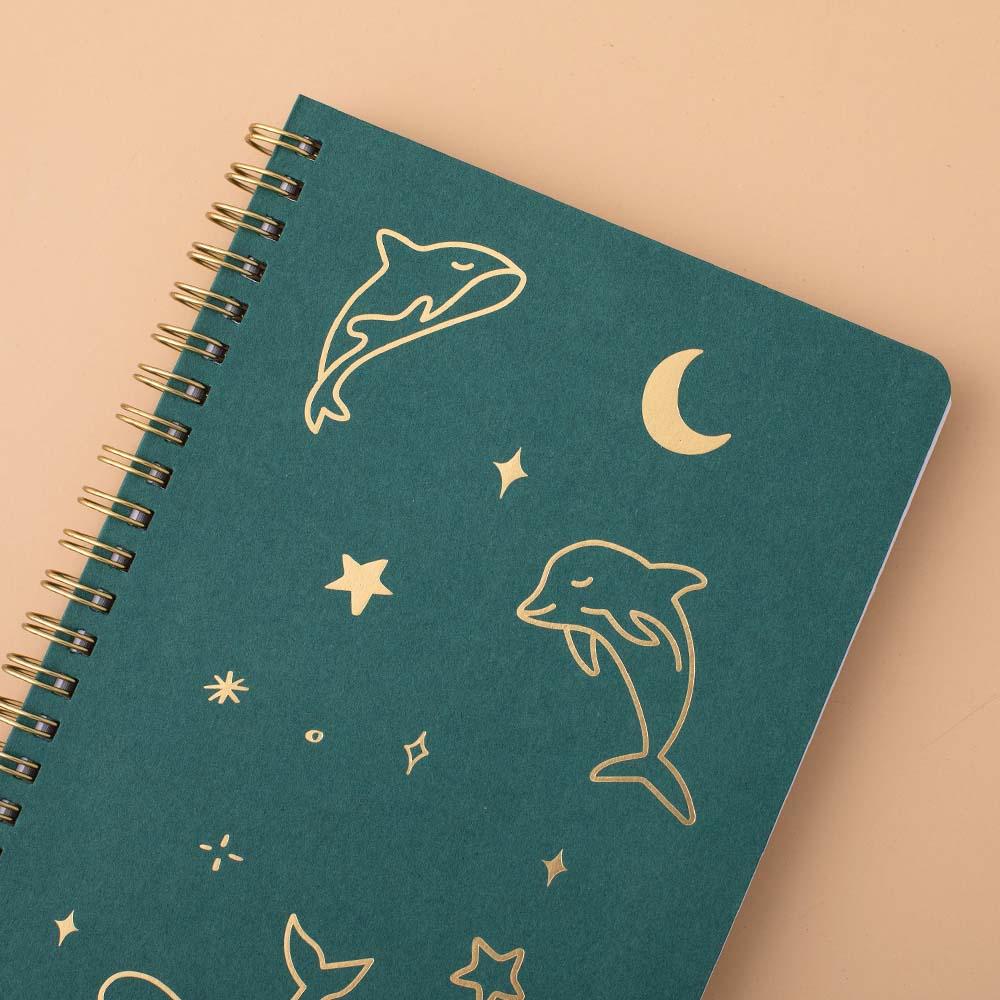Close up of Tsuki Ocean Edition Ring Bound notebook in deep teal on peach background