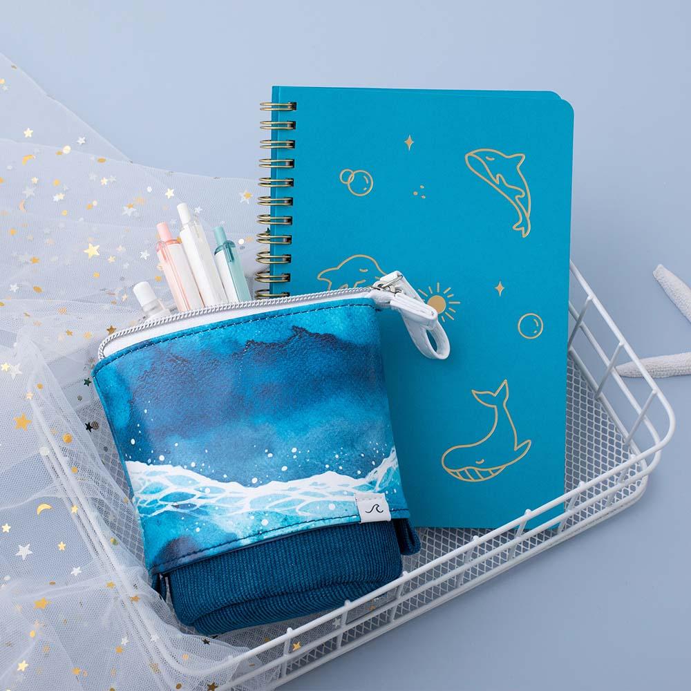 Tsuki Ocean Edition pop up standing pencil case in Ocean Blue with aqua blue Limited Edition Tsuki Ocean Ring Bound notebook in basket with pens in blue background