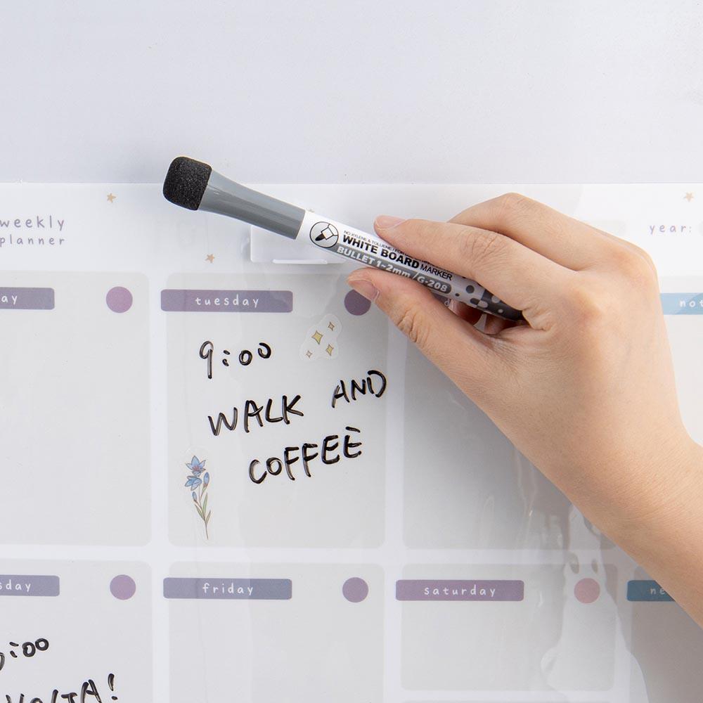 Close up of Tsuki Reusable Weekly Planner with whiteboard marker eraser and sticky pen holder held in hand on light grey surface