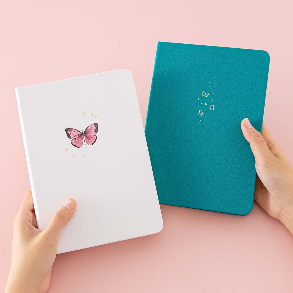 Tsuki Cloud White ‘Flutter + Dream’ Limited Edition Bullet Journal by Notebook Therapy x Pelinkan and Tsuki Teal Sky ‘Flutter + Dream’ Limited Edition Bullet Journal by Notebook Therapy x Pelinkan held in hands in pastel pink background