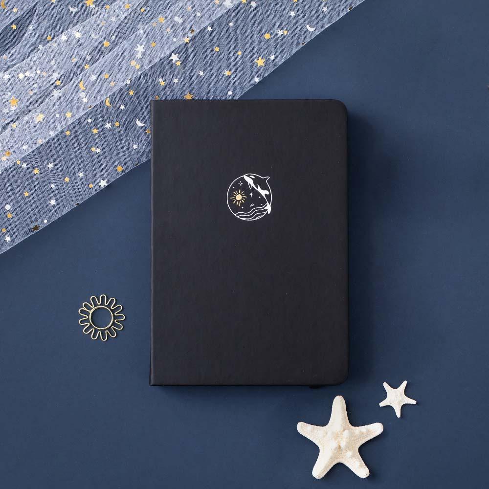 Tsuki deep black Playful Orca limited edition notebook at an angle with starfish and free sunshine gift on dark blue background