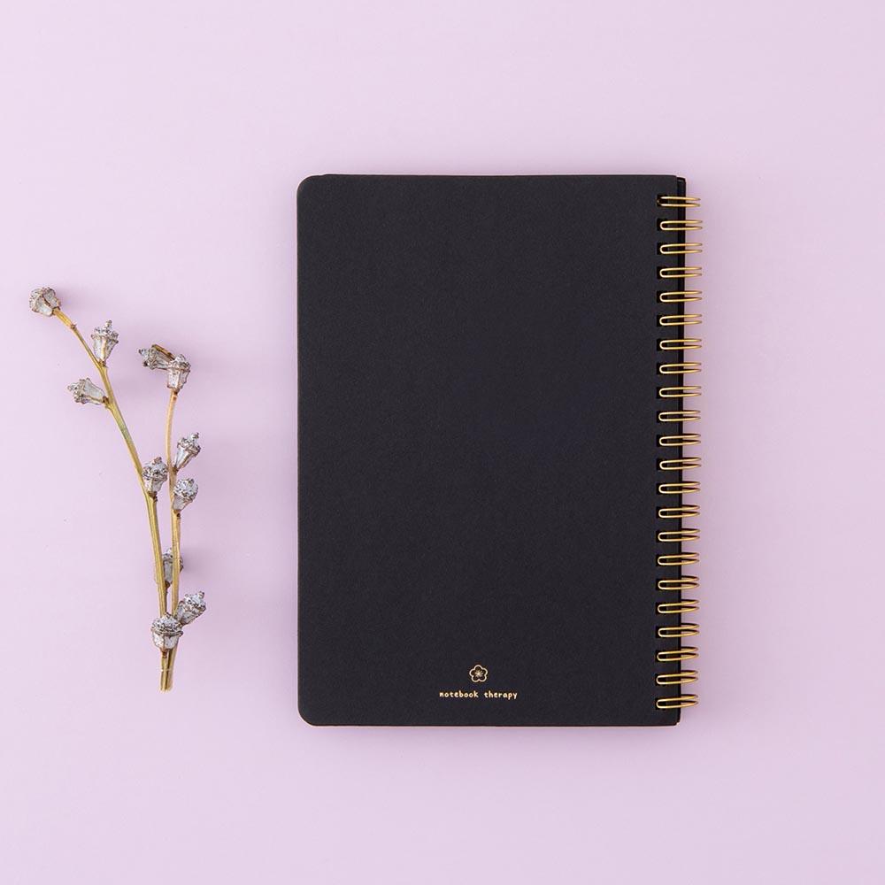 Back cover of Tsuki Black Paper Ringbound Bullet Journal with tree twig on lilac background