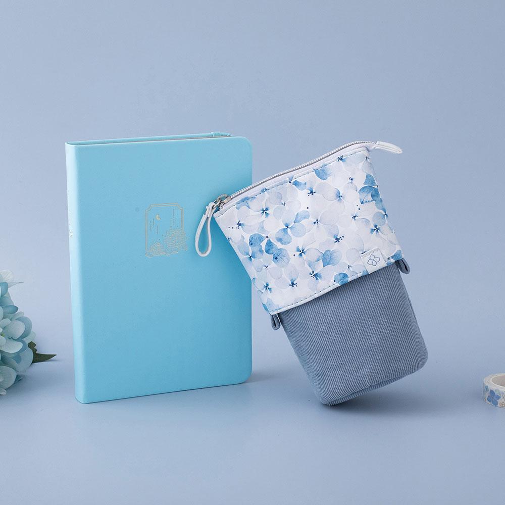 Tsuki Endless Summer Pop-Up Pencil case in Petal Blue with Tsuki Endless Summer Washi bullet journal in Petal Blue with light blue hydrangea flowers in light blue background