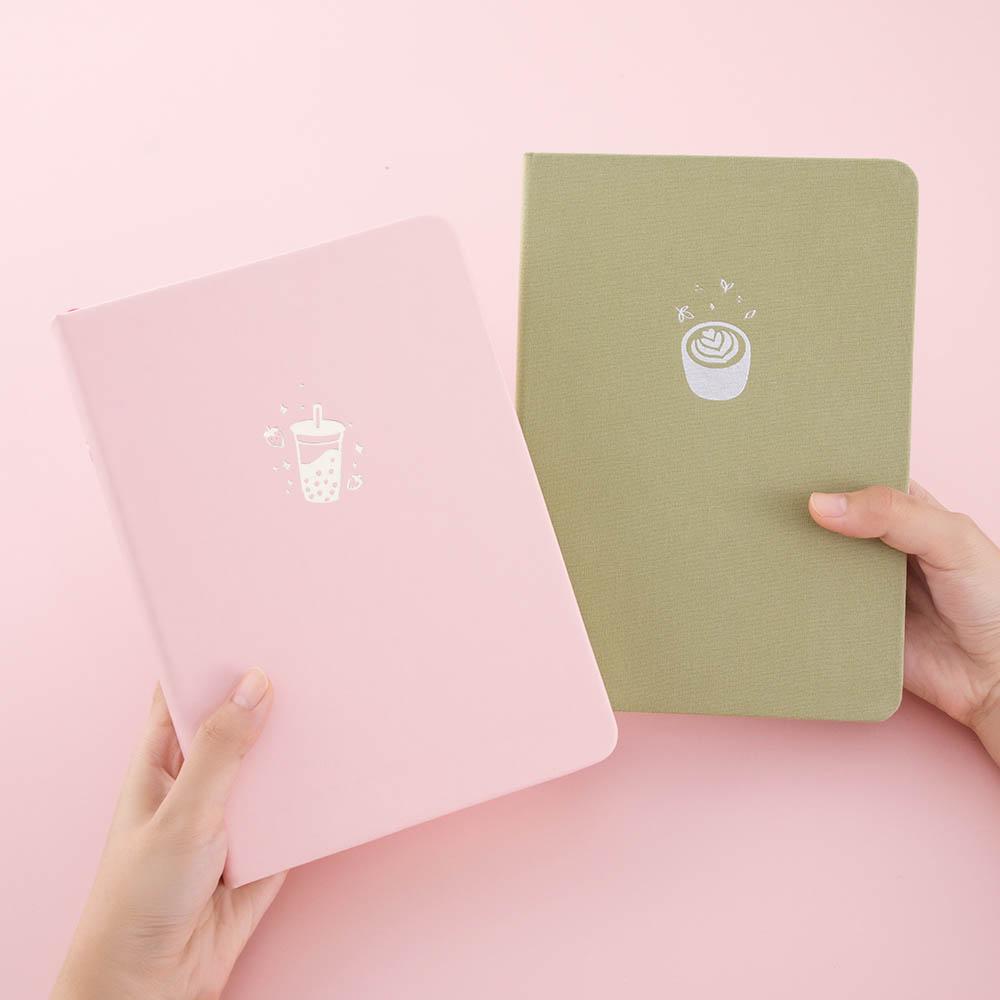 Tsuki ‘Ichigo’ Limited Edition Boba Bullet Journal and Tsuki ‘Matcha Matcha’ Limited Edition notebook held in hands in light pink background