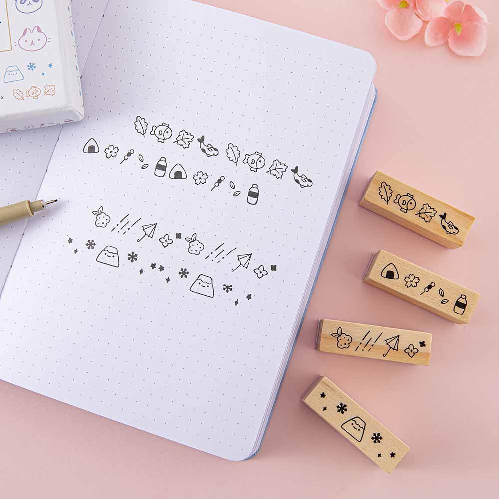 Tsuki ‘Four Seasons’ Bullet Journal Stamps by Notebook Therapy x Milkkoyo on open bullet journal page with pen and pink flower on petal pink background