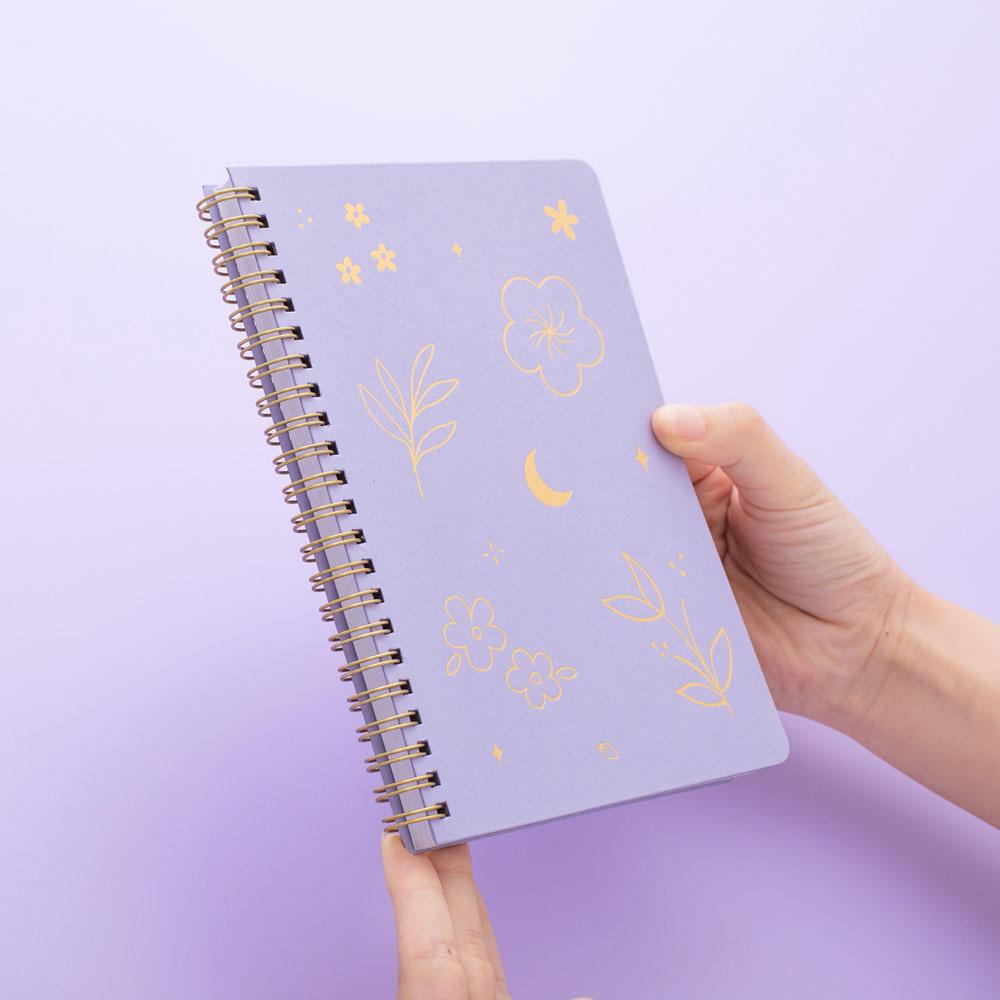 Tsuki lilac taro floral ringbound notebook held in hand at spiral spine angle in lilac background