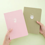 Tsuki ‘Ichigo’ Limited Edition Boba Bullet Journal and Tsuki ‘Matcha Matcha’ Limited Edition notebook held in hands in matcha green background