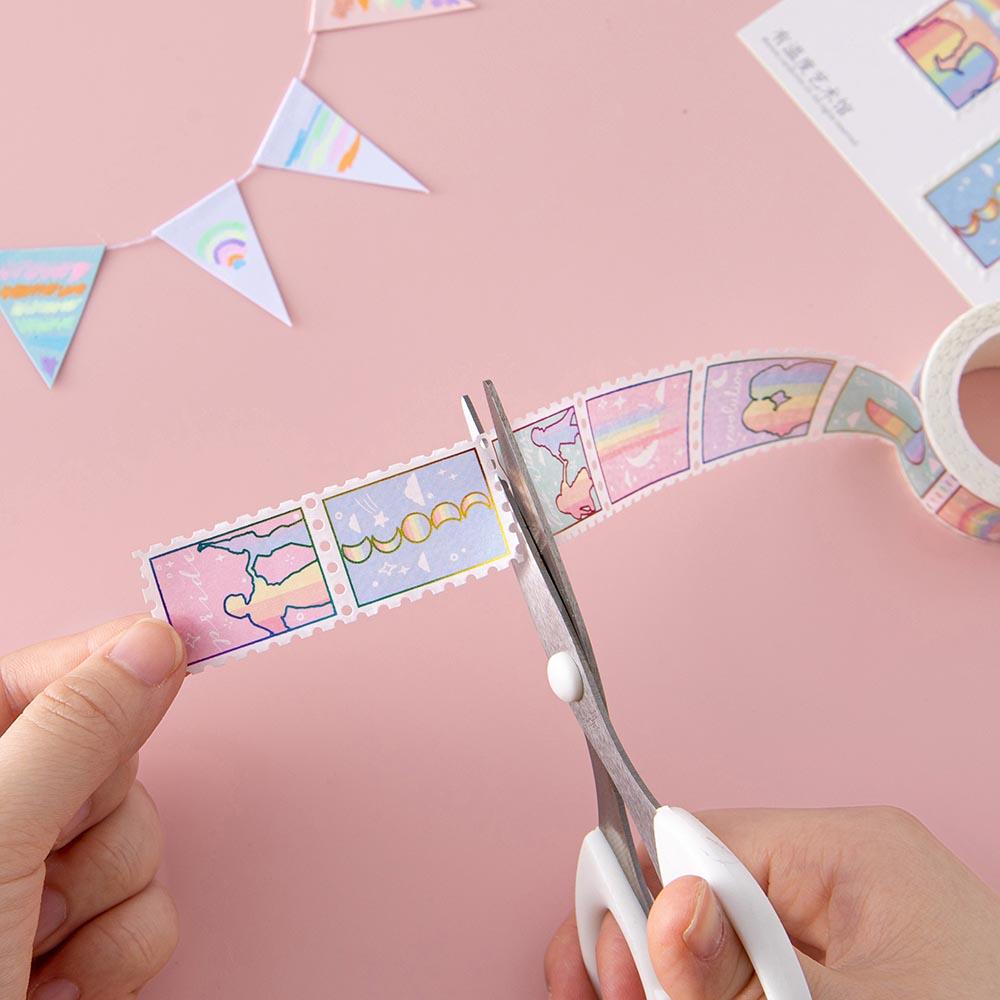 Tsuki Rainbow Pride Washi Tape being cut with scissors in hands with bunting on light pink background