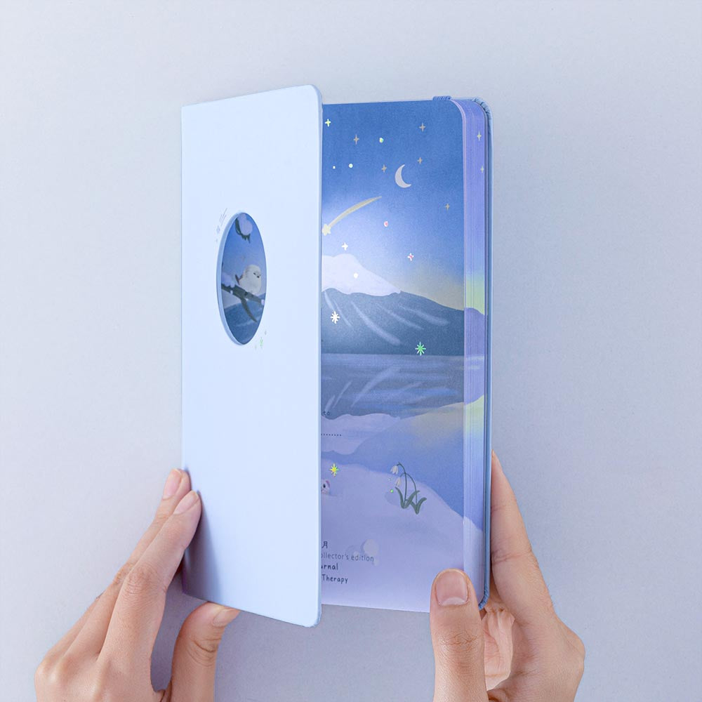 Tsuki Four Seasons Winter Collector’s Edition Bullet Journal held in hand at spine angle with open cut out cover in light blue background