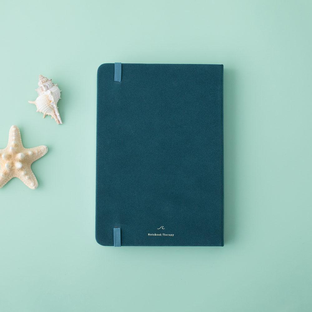 Focus on the back cover of Sea green velvet Tsuki Dolphin Days bullet journal with starfish and seashells on green background