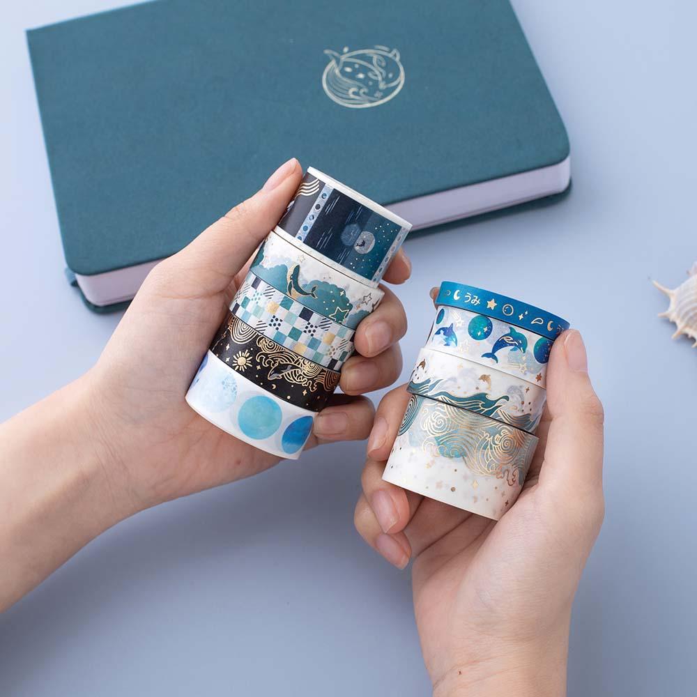 Tsuki Ocean Edition Washi Tapes held in hands with sea green Dolphin Days notebook in blue background