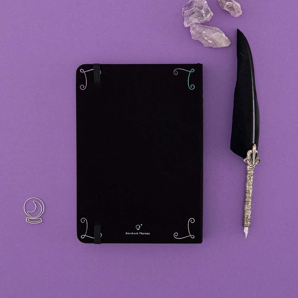Back cover of Tsuki ‘Moonlit Spell’ Limited Edition Holographic Bullet Journal with free bookmark gift with black feather quill and amethyst stones on purple background