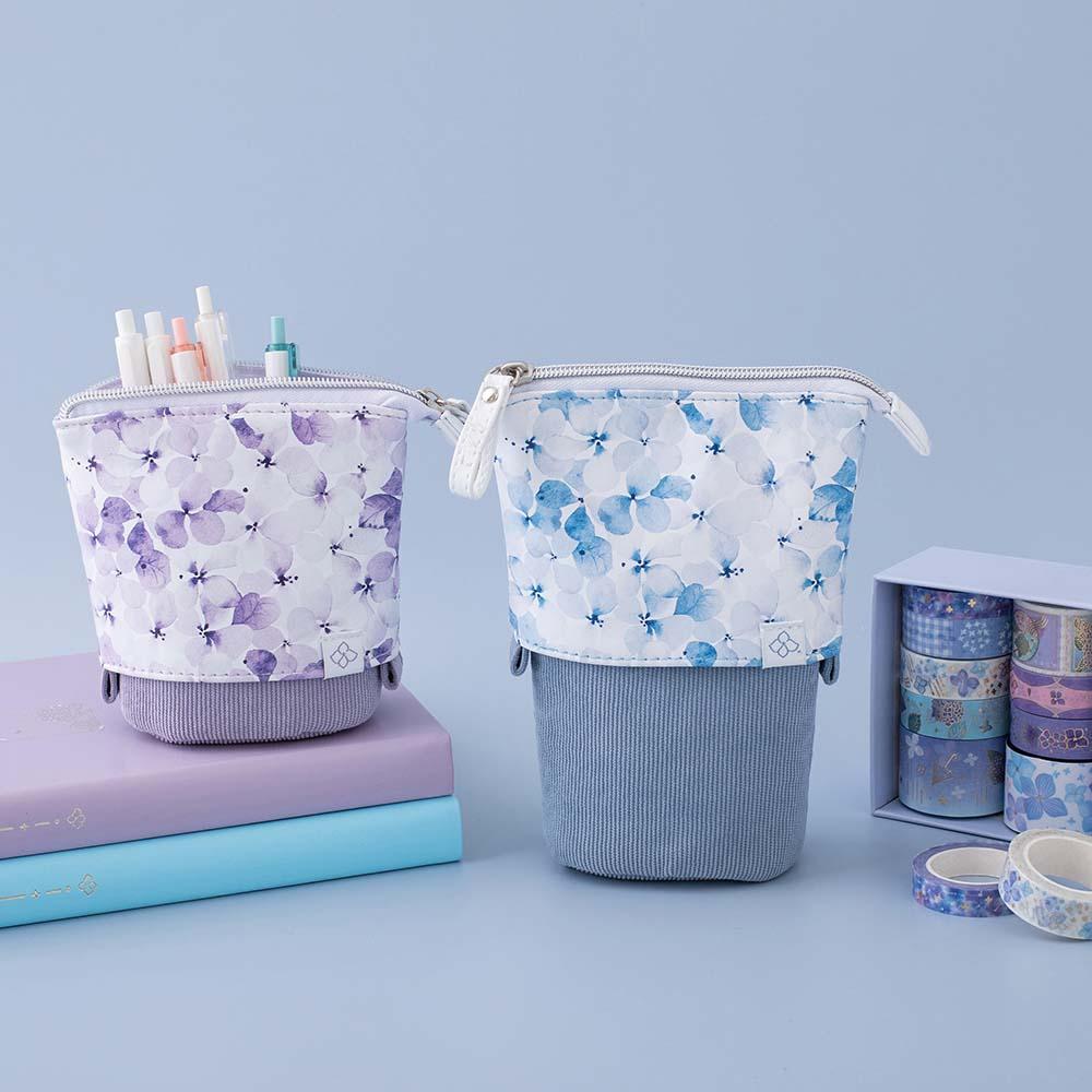 Tsuki Endless Summer Pop-Up Pencil cases in Lilac Bloom and Petal Blue on open bullet journal page with Tsuki Endless Summer Washi Tape roll and light blue hydrangea flowers on light blue background