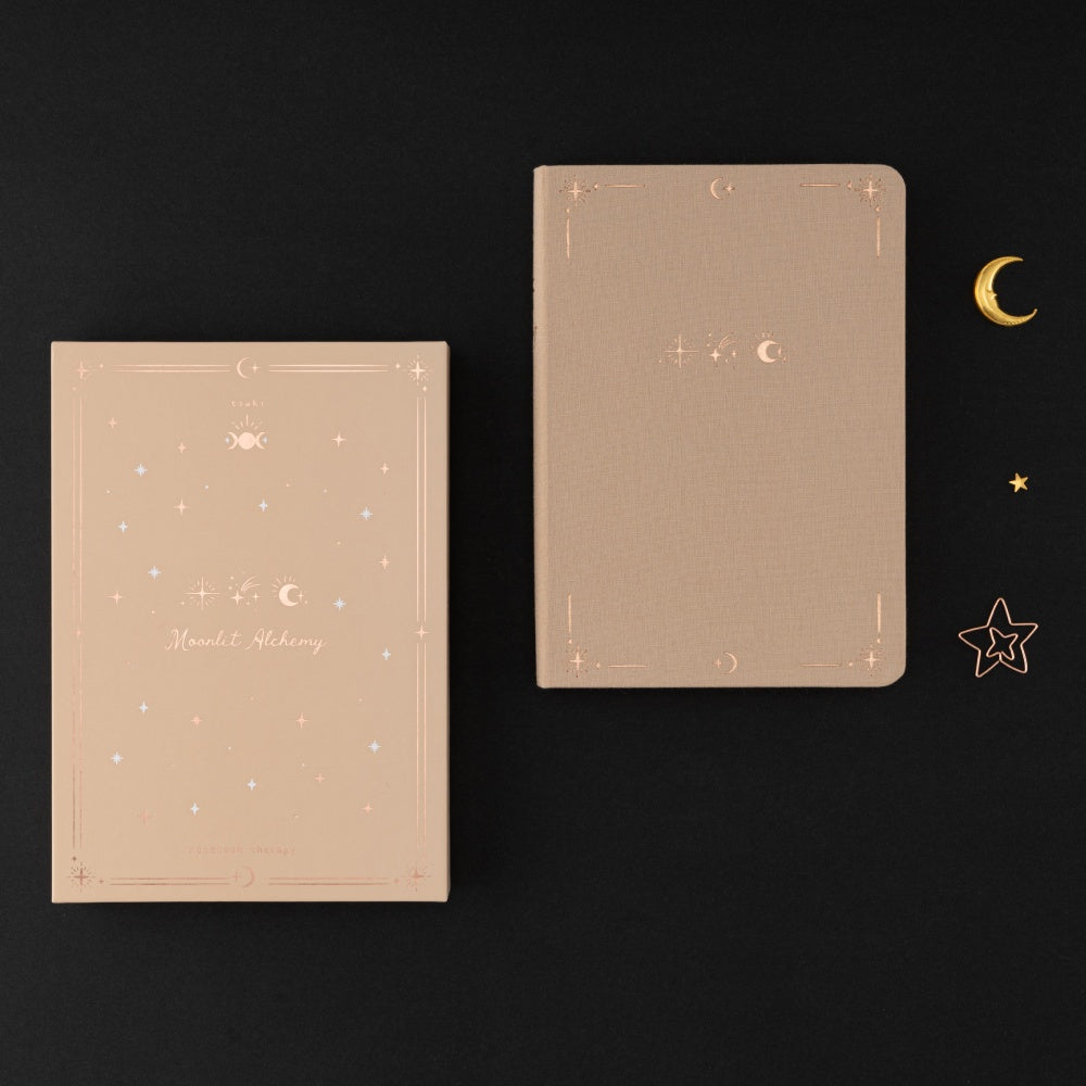 Flatlay of Moonlit Alchemy notebook box and Tsuki Stardust Dawn Bullet Journal on black background