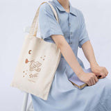Tsuki ‘Moonflower’ Limited Edition Tote Bag shown on model’s arm with ‘Full Bloom’ Limited Edition Bullet Journal on model’s knee on light blue background