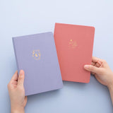 Tsuki ‘Full Bloom’ Limited Edition Bullet Journal with Tsuki ‘Suzume’ Limited Edition Notebook held in hands in lilac background