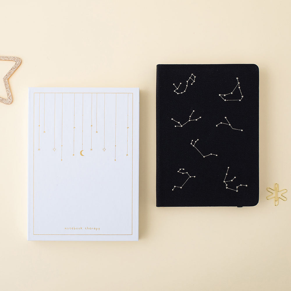 Flatlay of black constellations bullet journal with the tsuki gift box and the gold star paperclip