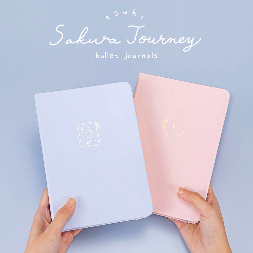 Tsuki ‘Lunar Blossom’ Limited Edition Bullet Journal with Tsuki ‘Sakura Journey’ Limited Edition Bullet Journal held in hands in light blue background