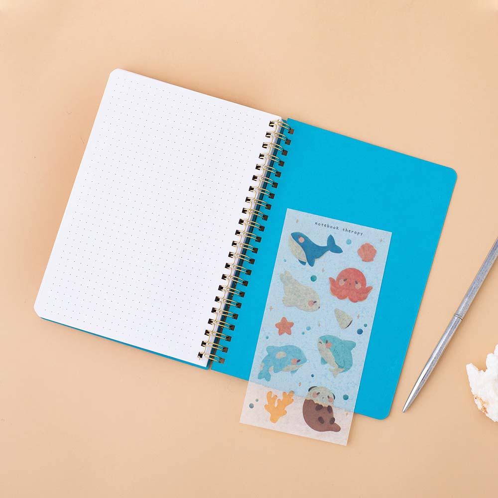 Tsuki Ocean Edition Ring Bound notebook in aqua blue with free sticker sheet and silver pen on peach background