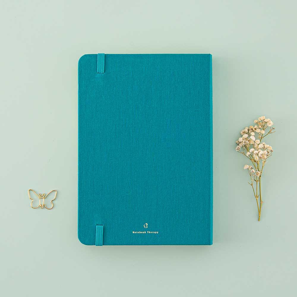 Back cover of Tsuki Teal Sky ‘Flutter + Dream’ Limited Edition Bullet Journal by Notebook Therapy x Pelinkan with free butterfly bookmark gift with free dried flowers on mint background
