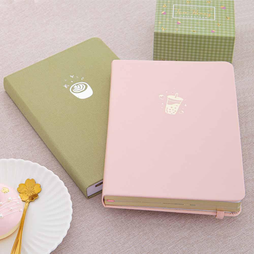 Tsuki ‘Ichigo’ Limited Edition Boba Bullet Journal and Tsuki ‘Matcha Matcha’ Limited Edition notebook and Tsuki ‘Matcha Ichigo’ Washi Tapes with teacup saucer and crystal glass on beige line covered table