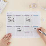 Tsuki Reusable Weekly Planner with dry erase marker held in hand with washi tape and sticky pen holder and calendar on buttermilk beige background