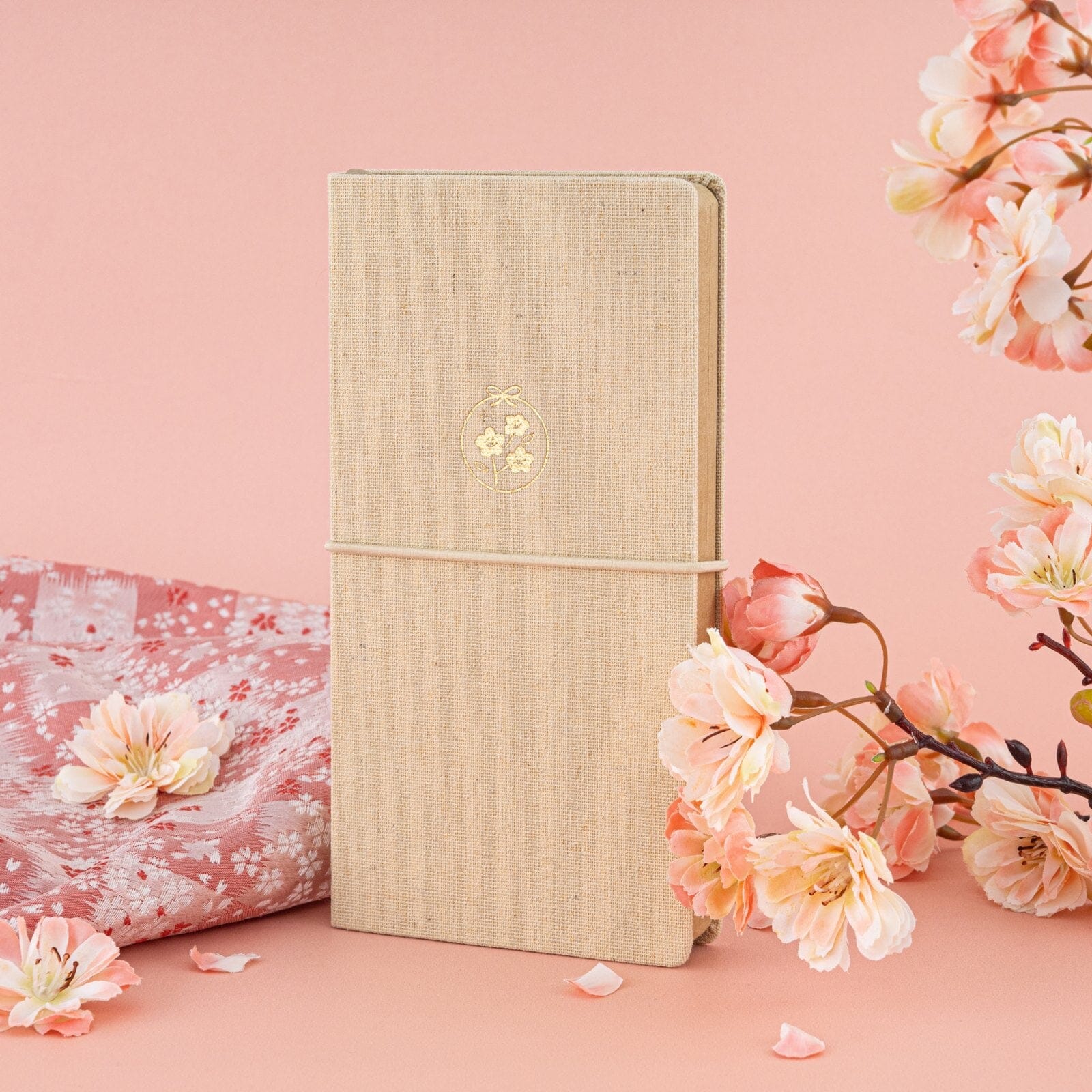 Tsuki ‘Sakura Breeze’ Kraft Paper Travel Notebook against pink background with cherry blossoms