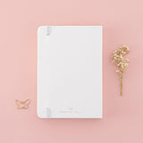 Back cover of Tsuki Cloud White ‘Flutter + Dream’ Limited Edition Bullet Journal by Notebook Therapy x Pelinkan with free butterfly bookmark gift with dried flowers on pastel pink background