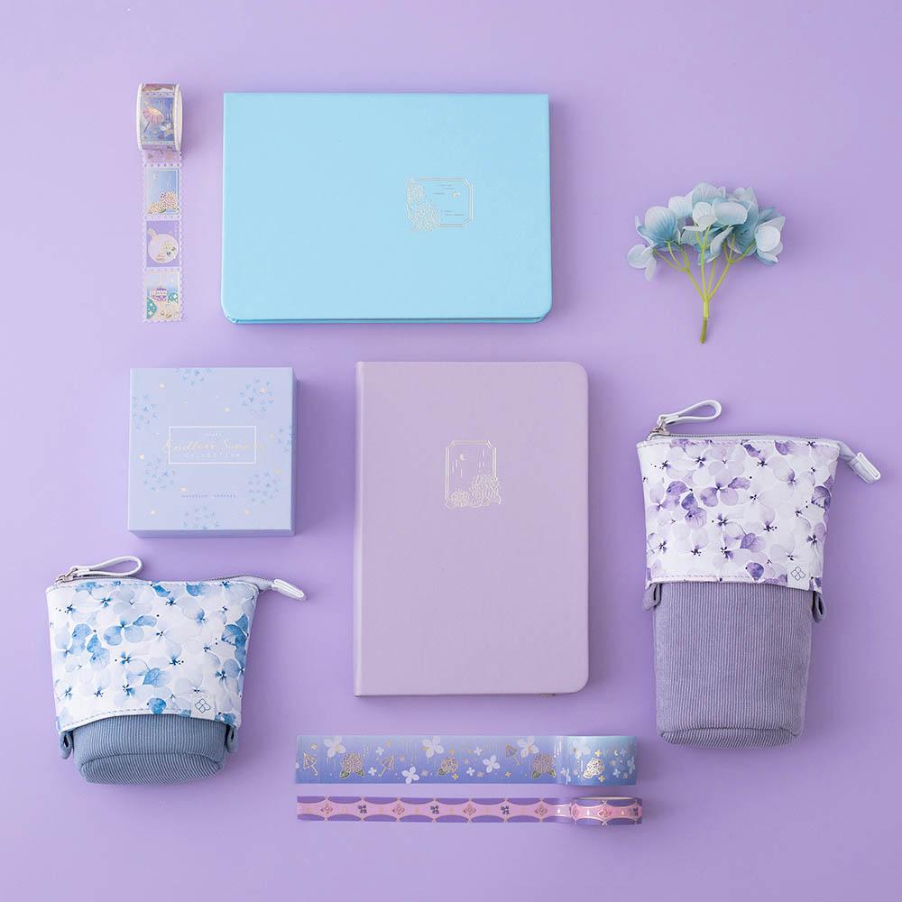 Tsuki Endless Summer Limited Edition Bullet Journals in Lilac Bloom and Petal Blue with Tsuki Endless Summer washi tape set and Tsuki Endless Summer Pop-Up Pencil cases and light blue hydrangea flowers on lilac background