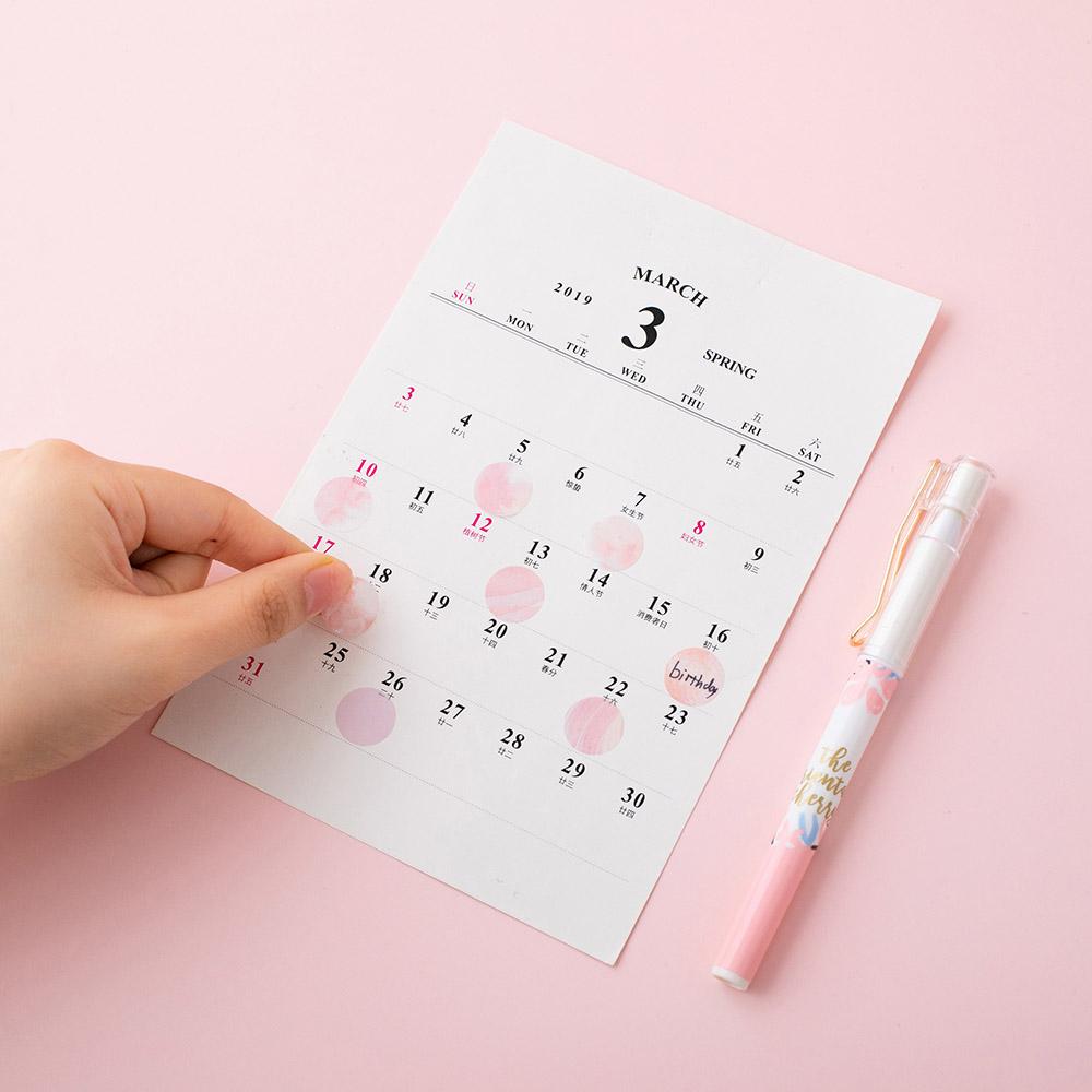 Tsuki 'Sakura Edition' Washi Petal Sticker Tape held in hand used on calendar with white pen on light pink background