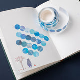 Close up of Tsuki Ocean Edition functional circle washi  tape on open notebook pages on dark blue background