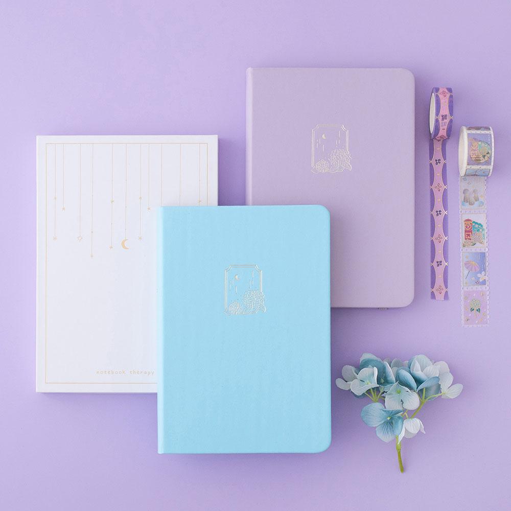 Tsuki Endless Summer Limited Edition Bullet Journals in Lilac Bloom and Petal Blue with eco-friendly gift box packaging and Tsuki Endless Summer washi tape rolls with light blue hydrangea flowers on lilac background