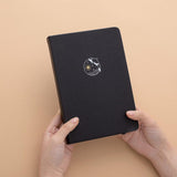 Tsuki deep black Playful Orca limited edition notebook held in hands in peach background