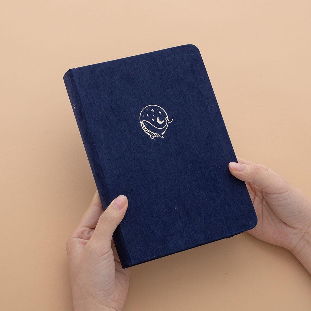 Tsuki deep blue textured vegan leather Gentle Giant luxury edition notebook held in hands at an angle in peach background