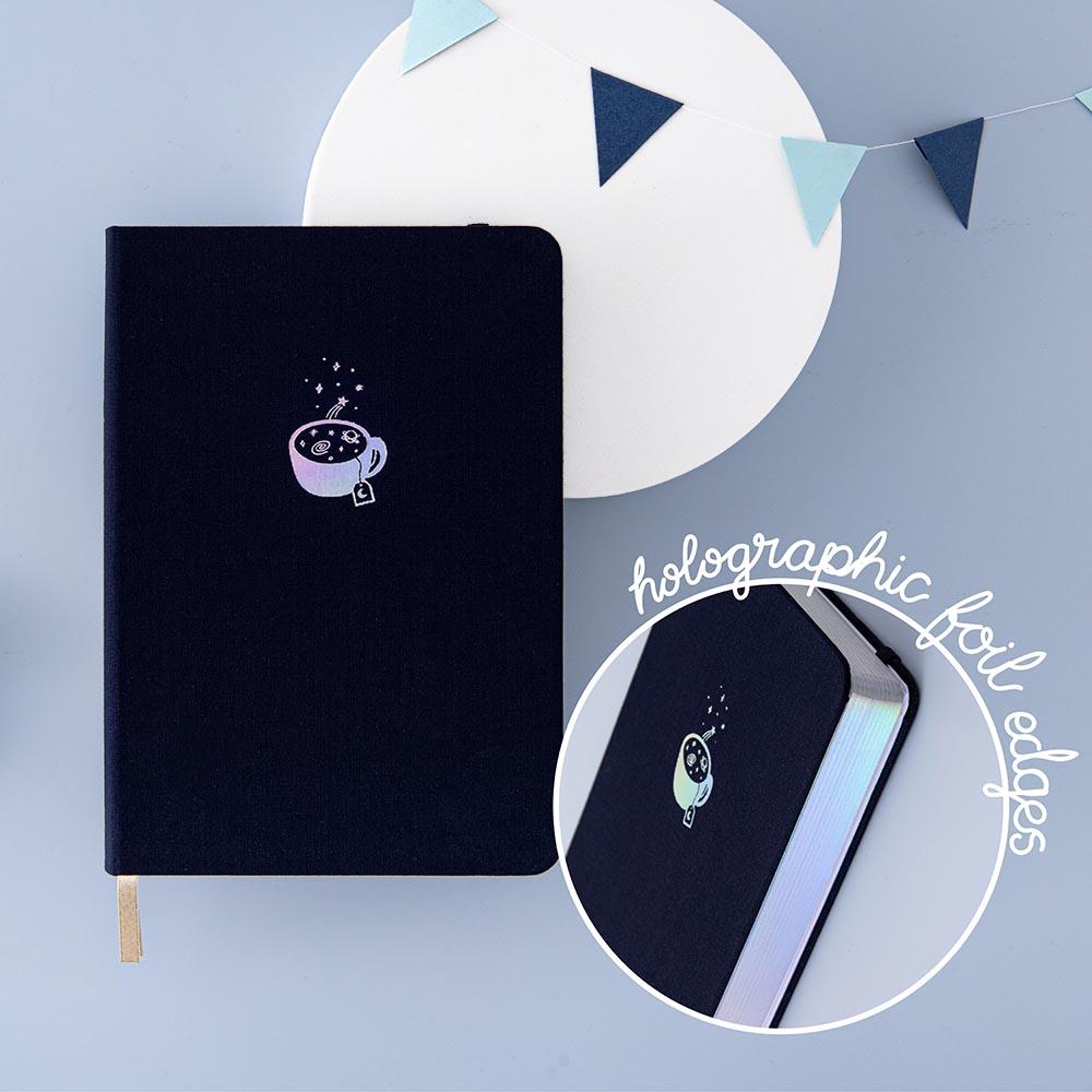 Tsuki ‘Cup of Galaxy’ Limited Edition Holographic Bullet Journal with holographic page edges on bright white circle with bunting on light blue background