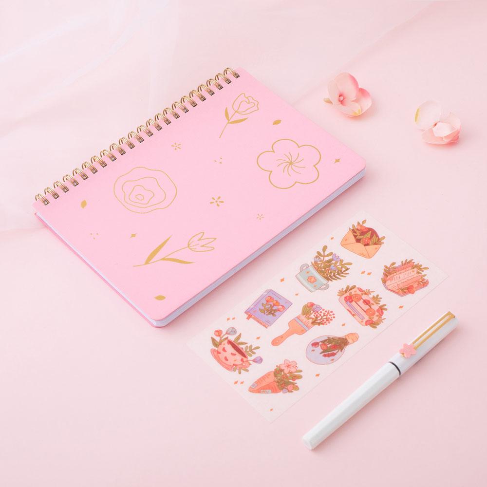 Sakura Pink Tsuki Floral ringbound bullet journal with free sticker sheet at an angle on pink background