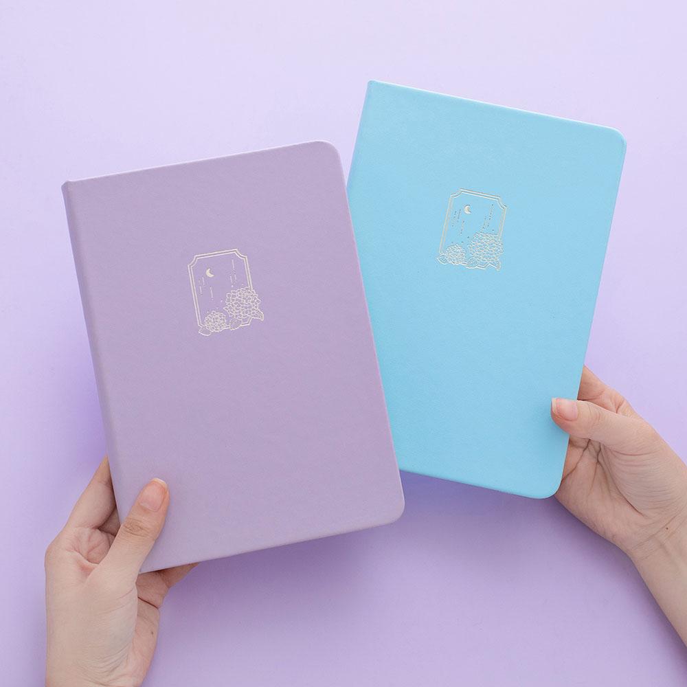 Tsuki Endless Summer Limited Edition Bullet Journals in Lilac Bloom and Petal Blue held in hands in lilac background