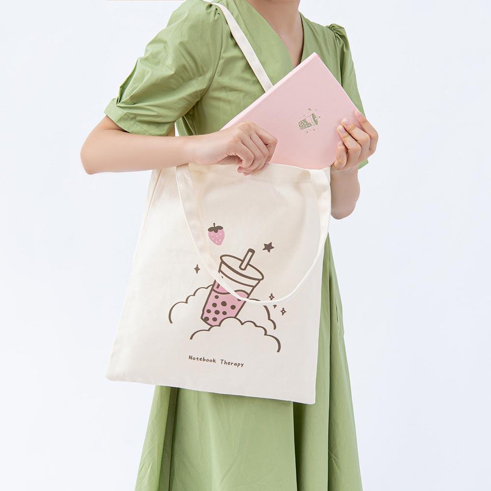 Tsuki ‘Ichigo’ Boba Tote Bag shown carried by model with Tsuki ‘Ichigo’ Limited Edition Boba Bullet Journal in light grey background