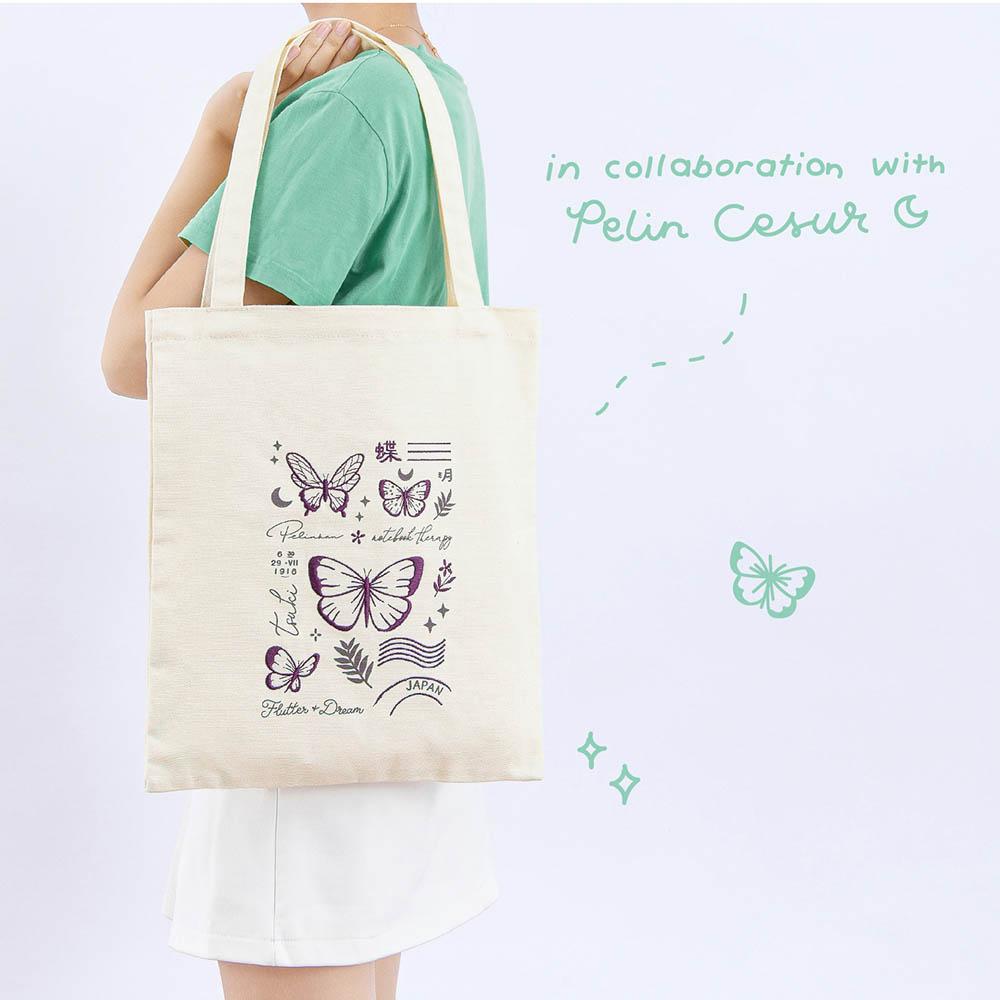 Tsuki ‘Flutter + Dream’ Tote Bag by Notebook Therapy x Pelinkan held over model’s shoulder in light grey background