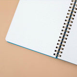 Close up of open page of Tsuki Ocean Edition Ring Bound notebook in aqua blue on peach background
