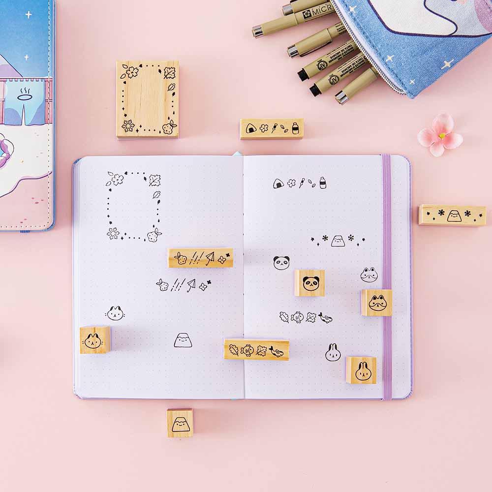 Tsuki ‘Four Seasons’ Bullet Journal Stamp Set by Notebook Therapy x Milkkoyo on open bullet journal spread with Tsuki ‘Four Seasons: Winter Edition’ Bullet Journal and Tsuki ‘Four Seasons’ Fuji Pop-Up Pencil Case with pink flower on petal pink background