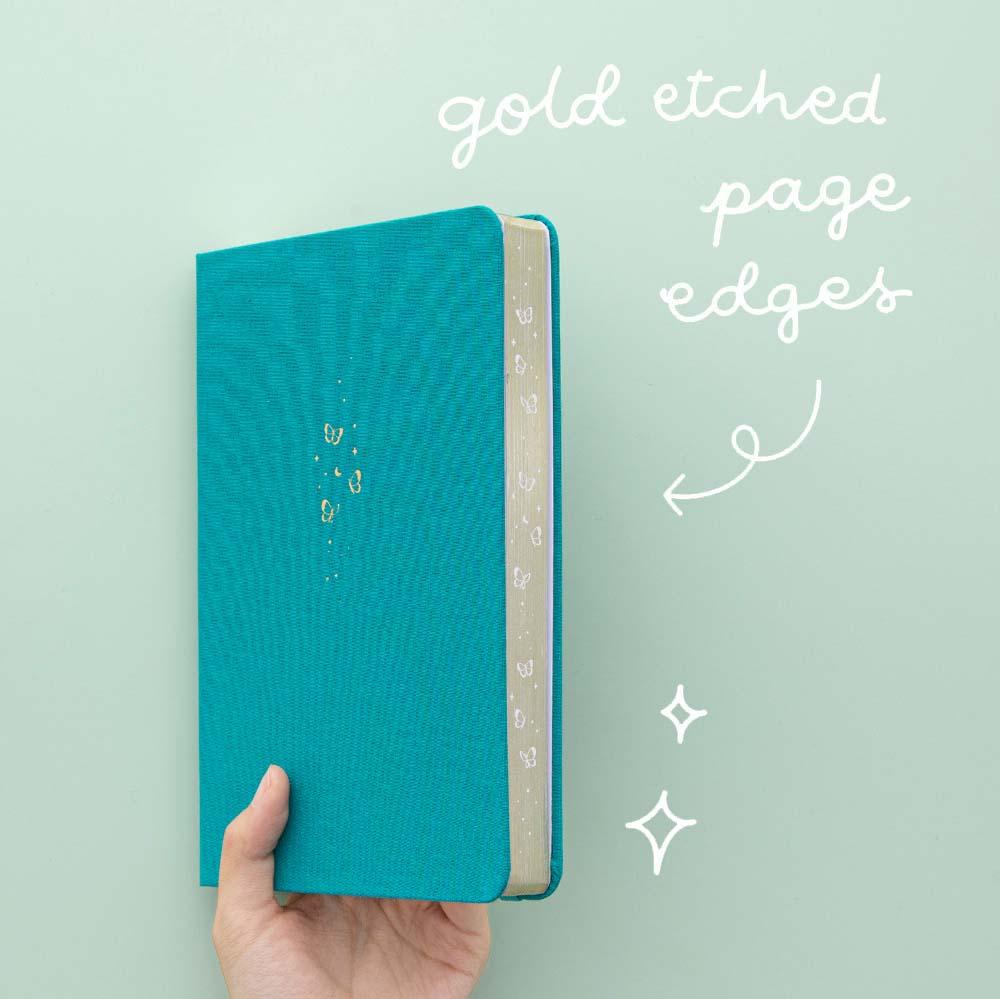 Tsuki Teal Sky ‘Flutter + Dream’ Limited Edition Bullet Journal by Notebook Therapy x Pelinkan with gold etched page edges held in hand at an angle in mint background