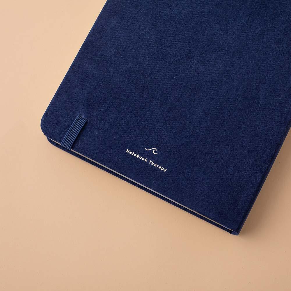 Close up of the back cover of deep blue textured vegan leather Tsuki Gentle Giant luxury edition bullet journal on peach background