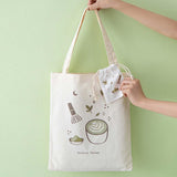 Tsuki ‘Matcha Matcha’ Tote Bag held in hands with free matching drawstring pouch in matcha green background
