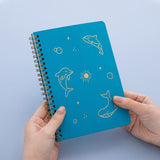 Tsuki Ocean Edition Ring Bound notebook in aqua blue held in hands in blue background