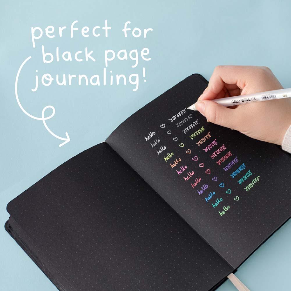 Gelly Roll Pen in white held in hand over open Tsuki Black Paper Limited Edition Hardcover Bullet Journal on light teal background
