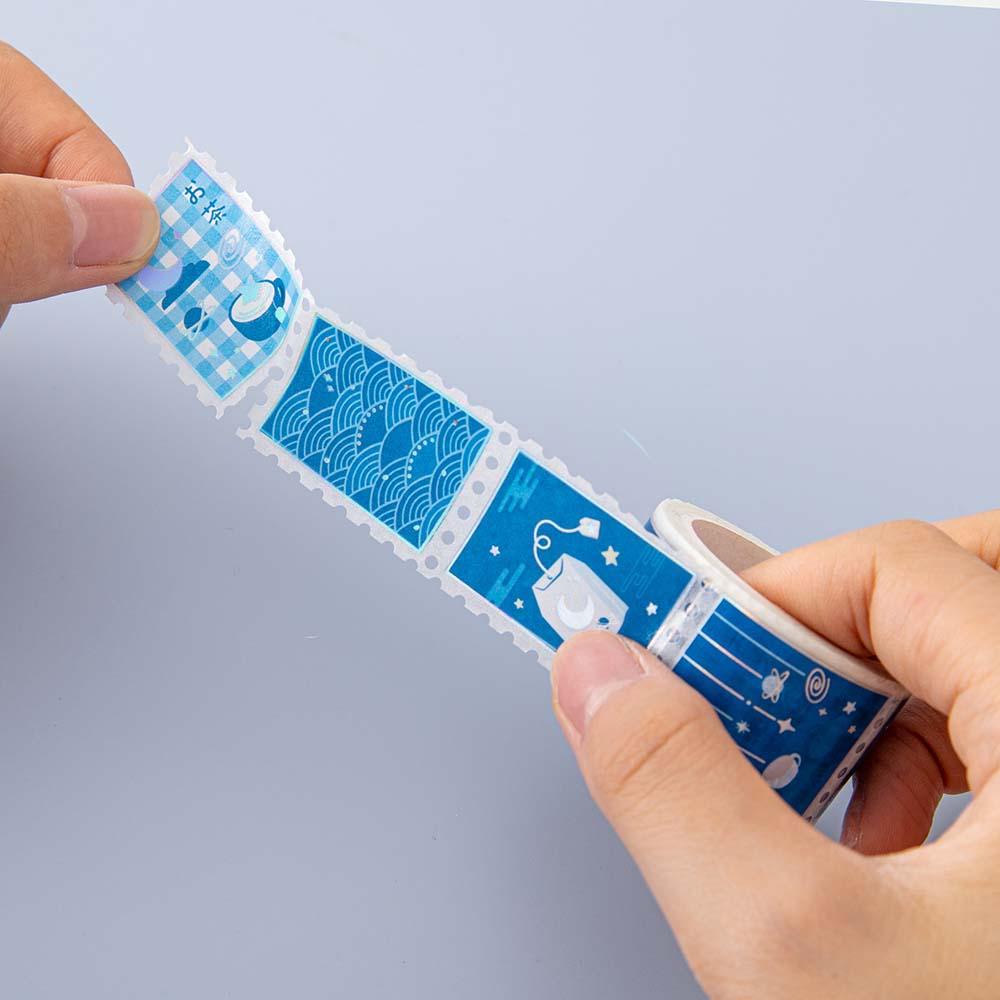 Close up of Tsuki ‘Cup of Galaxy’ stamp Washi Tape held in hands in light blue background